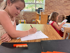 Learner writing in her notebook alongside Montessori materials